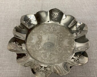 May include: A silver, scalloped serving dish with an ornate, embossed design. The dish is made of metal and has a shiny finish.