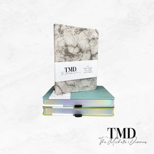 Op de afbeelding: Een stapel van drie notitieboekjes met een marmermotief op de omslag. Het bovenste notitieboekje heeft een wit label met de tekst "TMD The Michelle Diaries A5 Dot Grid 160 GSM 100 Pages". De twee onderste notitieboekjes hebben een lichtblauwe en een lichtgroene omslag.