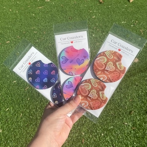 May include: Four car coasters with different heart designs. The coasters are made of a soft, absorbent material and are perfect for protecting your car's cup holders from spills and stains. The coasters are packaged in a clear plastic bag with a header card that reads "Car Coasters Handmade with love".