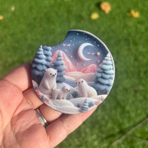 May include: A round, blue and white coaster with a snowy mountain scene and three polar bears. The coaster has a crescent moon and stars in the sky.