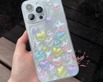 May include: A clear phone case with a glittery, iridescent finish. The case is decorated with colorful hearts and stars.