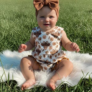 Adorable western themed baby girl outfit featuring a floral highland cow design and pom trim, perfect for summer adventures, family photos, and everyday wear. A charming baby clothing choice and memorable baby shower gift idea.