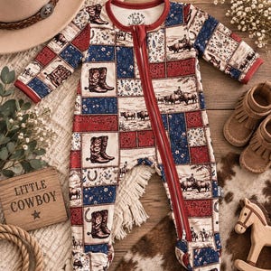 May include: A long-sleeved, footed baby sleepsuit featuring a patchwork print of cowboy boots, bison, horses, and paisley patterns in red, blue, and cream. The garment has a full-length front zip and a red trim around the neckline and cuffs.