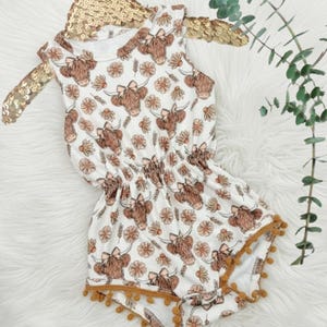Close up of a baby girls floral highland cow pom romper western summer outfit with detailed cow print, floral accents, and soft comfy material. Ideal cute clothes for girls and a unique baby shower gift or special baby gift for girls.