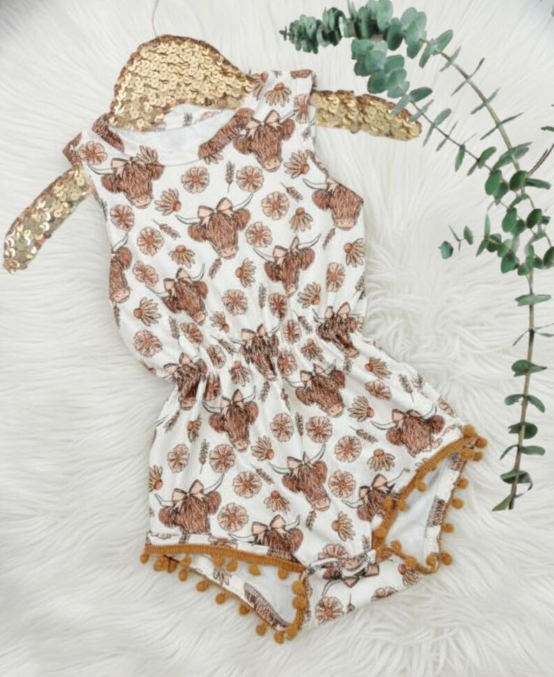 Close up of a baby girls floral highland cow pom romper western summer outfit with detailed cow print, floral accents, and soft comfy material. Ideal cute clothes for girls and a unique baby shower gift or special baby gift for girls.