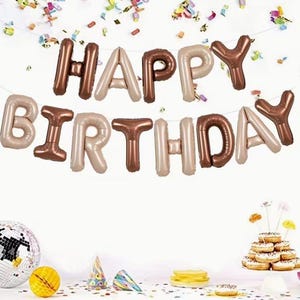 May include: A birthday party decoration featuring foil balloons spelling "HAPPY BIRTHDAY" in brown and beige. The scene includes confetti, a disco ball, a yellow ball, party hats, and donuts.