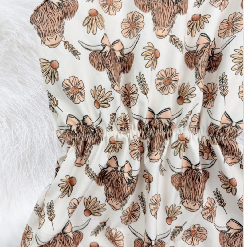 Floral farm inspired baby girl romper with highland cow artwork and pom details, styled as a western summer outfit. Soft baby clothing perfect for warm days, photos, birthdays, and gifting for baby girls and baby showers.