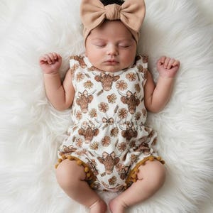 Baby girl wearing a floral highland cow pom romper styled as a western summer outfit, featuring soft breathable fabric and cute country charm. Perfect baby clothing for warm weather, photoshoots, vacations, and a thoughtful baby gift for girls or baby shower gift.