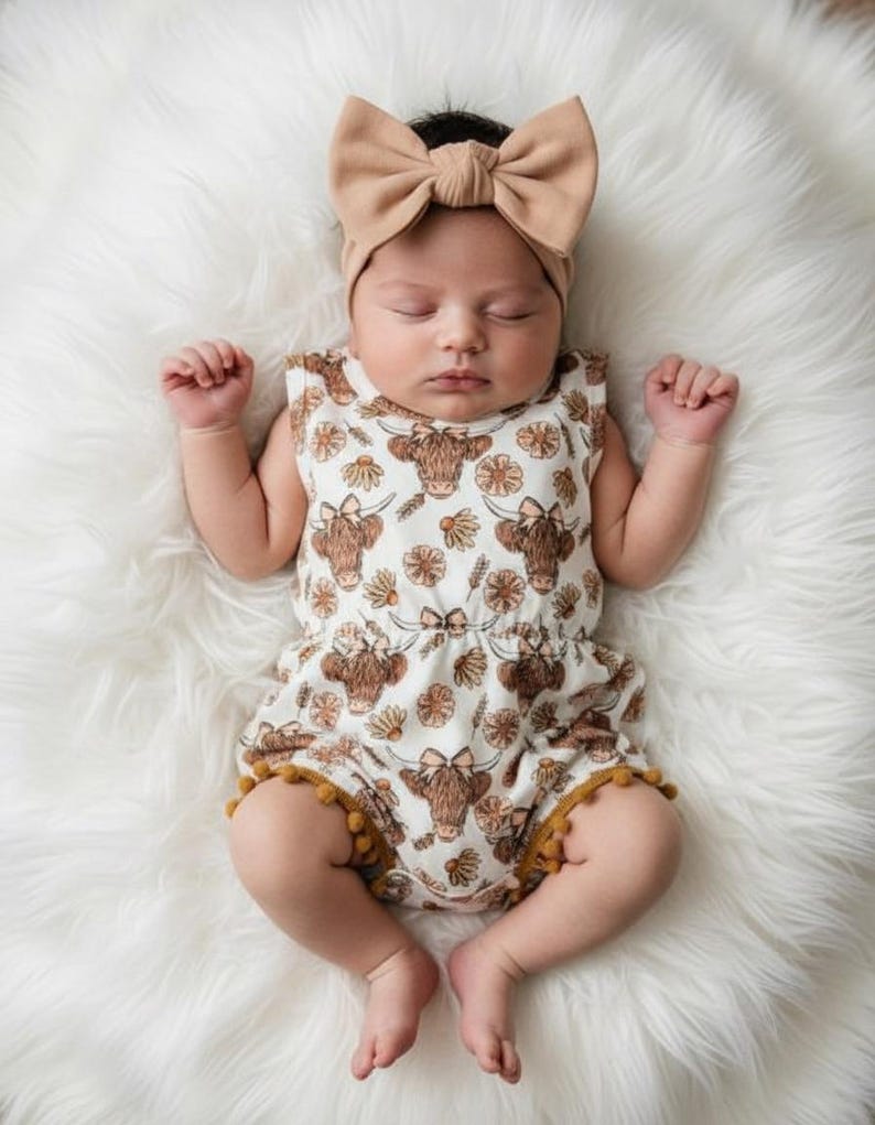Baby girl wearing a floral highland cow pom romper styled as a western summer outfit, featuring soft breathable fabric and cute country charm. Perfect baby clothing for warm weather, photoshoots, vacations, and a thoughtful baby gift for girls or baby shower gift.