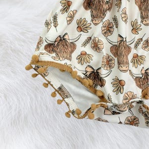 Western summer baby girl outfit featuring a floral highland cow romper, breathable fabric, and playful pom trim. A beautiful baby clothing piece that works as a baby gift for girls, newborn present, or baby shower gift.