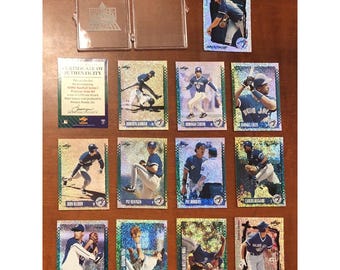 May include: A collection of 12 Toronto Blue Jays baseball cards featuring various players from the 1990s. The cards are holographic and have a blue and green color scheme. The cards feature players such as John Olerud, Pat Hentgen, and Carlos Delgado.