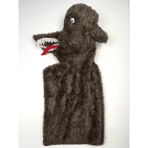 May include: A brown plush wolf puppet with white teeth and a red tongue. The puppet has a long body and a head with two small ears and a single eye. The puppet is made of a soft, furry material.