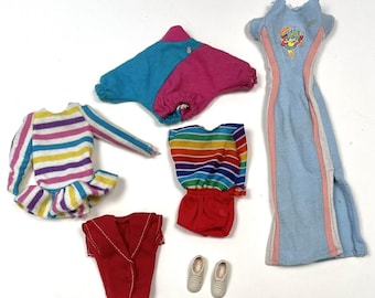 May include: A collection of vintage doll clothes, including a light blue dress with a cartoon graphic, a red vest, and colorful striped tops and bottoms. Also included are a pair of white sneakers and blue and pink shorts.
