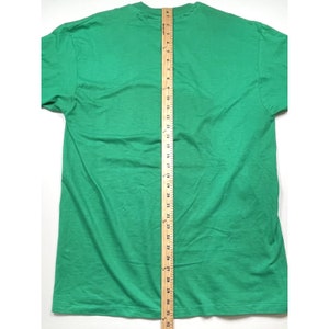 K&ouml;nnte beinhalten: Ein einfarbiges gr&uuml;nes T-Shirt mit Rundhalsausschnitt und kurzen &Auml;rmeln. Das Shirt liegt flach und wird mit einem Lineal gemessen.