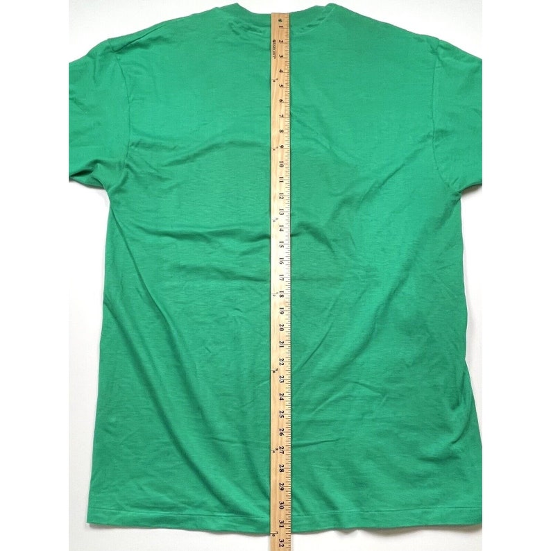 K&ouml;nnte beinhalten: Ein einfarbiges gr&uuml;nes T-Shirt mit Rundhalsausschnitt und kurzen &Auml;rmeln. Das Shirt liegt flach und wird mit einem Lineal gemessen.