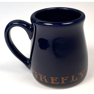 May include: A navy blue ceramic mug with a curved handle. The mug has a glossy finish and the word "FIREFLY" is printed in a copper color on the lower part of the mug.