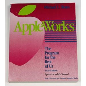 May include: A vintage book titled "AppleWorks" with a large apple graphic. The cover is primarily red and pink with green text and a green apple leaf. The book's subtitle reads "The Program for the Rest of Us."