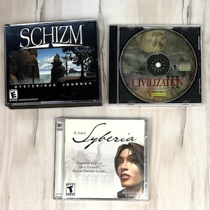 May include: Three PC game cases including Schizm: Mysterious Journey with a landscape cover, Sid Meier's Civilization III with a visible game disc inside, and B. Sokal Syberia featuring a character portrait and the text Uncover a Secret on a Journey.