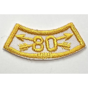 May include: A white patch with a yellow border and two yellow arrows pointing in opposite directions. The number "80" is embroidered in yellow in the center of the patch.