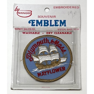 May include: Embroidered souvenir emblem featuring a blue circle with a ship illustration and the words "Plymouth, Mass" and "Mayflower." The emblem is packaged in a clear plastic sleeve with the text "Washable - Dry Cleanable."
