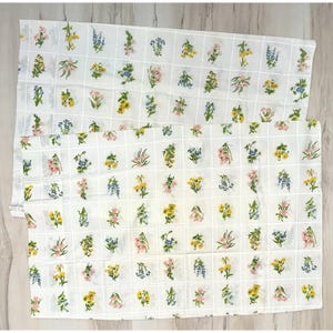 May include: A white fabric featuring a grid pattern with small, colorful floral illustrations in each square. The flowers appear in various shades of yellow, pink, blue, and green, arranged in a repeating, organized layout across the textile surface.