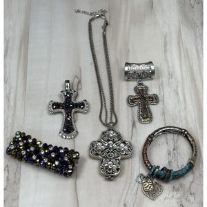May include: A collection of religious jewelry, including cross pendants, a bracelet, and a ring. The cross pendants feature intricate designs with silver and iridescent accents. The bracelet is made of iridescent beads, and the ring has a decorative design.