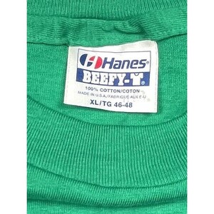 K&ouml;nnte beinhalten: Ein gr&uuml;nes Hanes Beefy-T T-Shirt mit einem wei&szlig;en Etikett, auf dem steht "Hanes Beefy-T 100% Baumwolle/Coton Hergestellt in den USA/Fabriqu&eacute; aux E-U XL/TG 46-48".