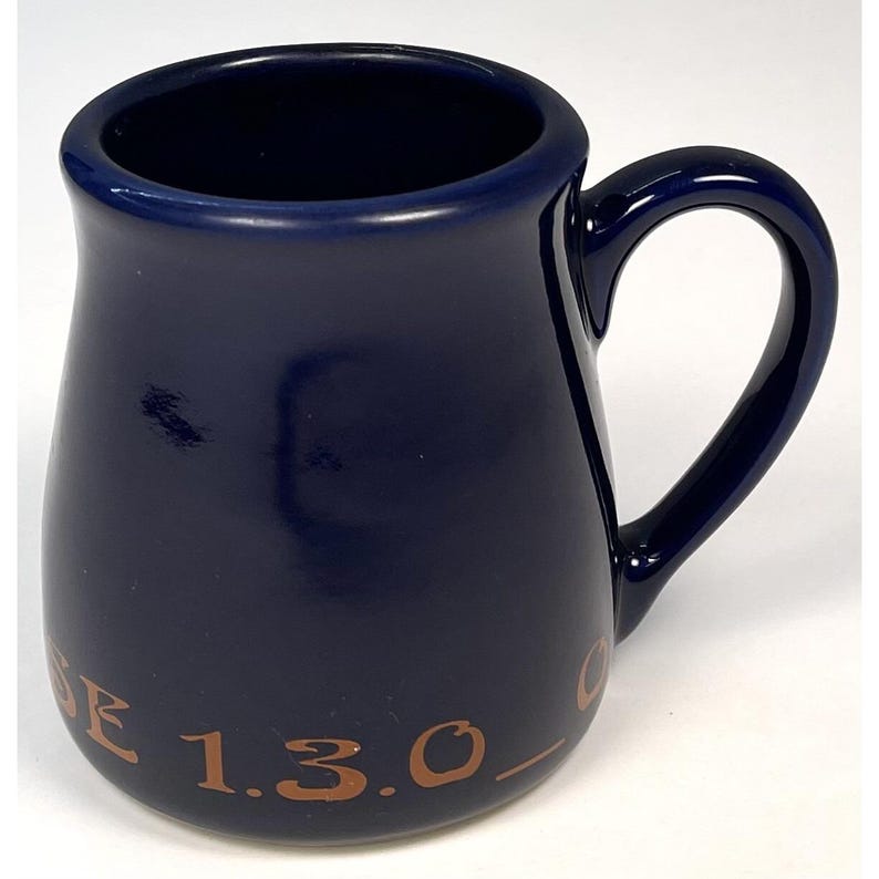 May include: A navy blue ceramic mug with a curved handle. The mug has a slightly flared shape and features the text "E 1.3.0." in a brown color on the side. The mug is designed for beverages.