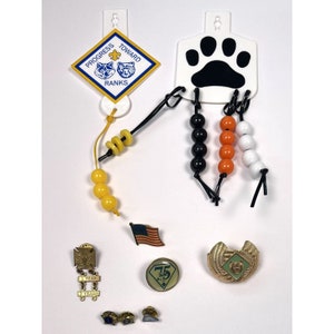 May include: A set of Boy Scout badges and beads. The badges are yellow and blue with the words "Progress Toward Ranks". The beads are yellow, black, orange, and white.