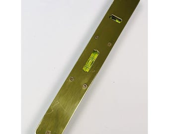May include: A brass-colored level tool with three bubble vials for measuring horizontal and vertical alignment. The level has a rectangular shape with rounded ends and several screw heads. The vials are filled with a green liquid.