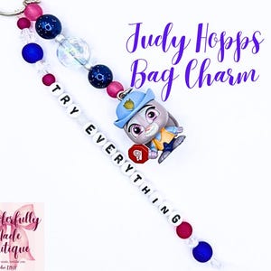 May include: A bag charm featuring a Judy Hopps character figurine wearing a blue hat, accented with dark blue, pink, and clear beads. A string of white letter beads spells out TRY EVERYTHING, accompanied by a small red stop sign charm.
