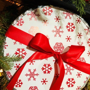 May include: A white pie pan with a red ribbon tied around it. The pan is decorated with a snowflake pattern.