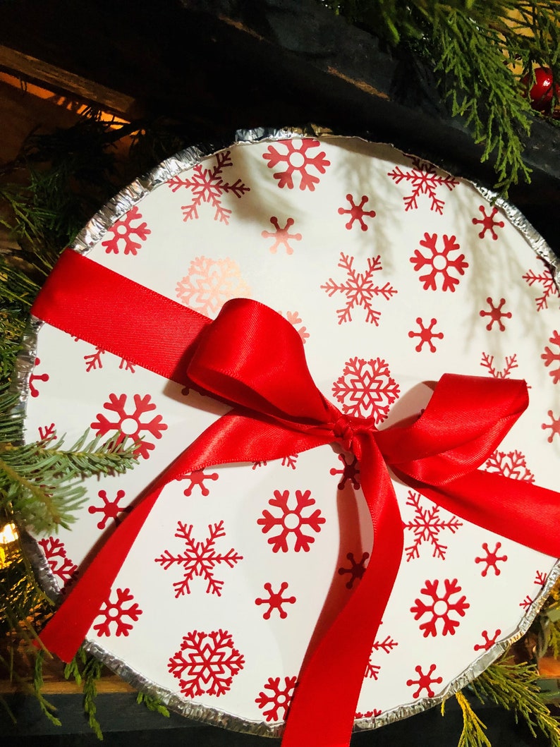 May include: A white pie pan with a red ribbon tied around it. The pan is decorated with a snowflake pattern.