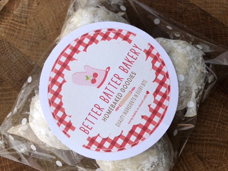 May include: A white round label with red and white checkered pattern. The label has the text "Better Batter Bakery" and "Homebaked Goodies" with the tagline "Quality Ingredients in Every Bite" and "every batch is mixed with love". The label is on a clear plastic bag with white polka dots, containing three white powdered cookies.