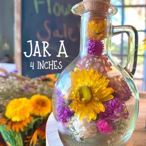 May include: A clear glass jar, approximately 10 cm tall, filled with dried yellow, purple, and white flowers. The jar has a cork stopper and a handle. Text on the image reads "Jar A" and "4 inches".