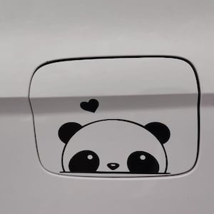 May include: A white car fuel door with a black and white panda bear graphic and a black heart above the panda's head. The panda has large eyes and round ears.