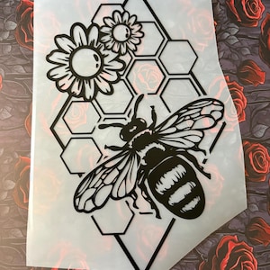 Könnte beinhalten: Schwarz-weißes Bienen- und Wabenmuster mit zwei Blumen. Die Biene ist zentriert, mit einem Wabenmuster und Blumen darüber. Das Design befindet sich auf einem durchscheinenden Blatt.