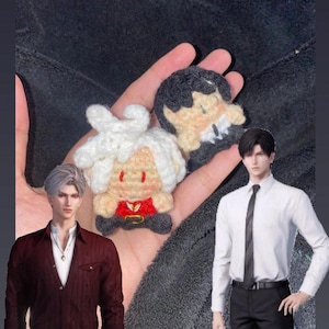 May include: Handmade crochet dolls in the image. One doll has white hair, a red top, and black pants. The other doll has black hair and a black suit. The dolls are held in a hand.
