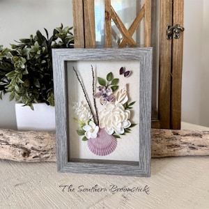 May include: A white ceramic mug with a black handle and the text "But First, Coffee" in a bold, black font. The mug is set against a blurred background, suggesting a cozy setting.