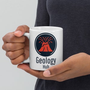 Puede incluir: Taza de café de cerámica blanca con un gráfico de volcán negro y rojo y el texto "Geology Hub".