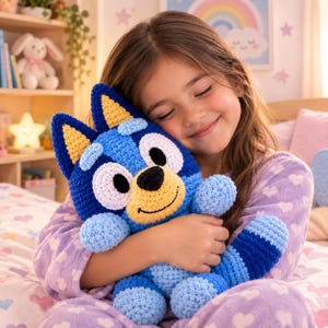 May include: A crochet plush toy of a blue dog character with large white eye patches, a black nose, a yellow muzzle, and pointed ears with yellow centres. The toy features a textured yarn construction in shades of blue, light blue, and yellow.