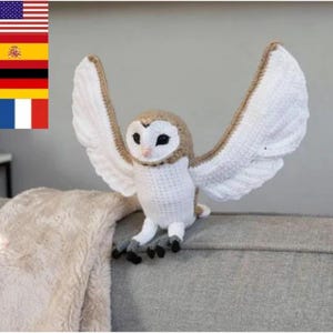 Peut inclure: Une figurine de chouette effraie au crochet avec une poitrine blanche, une tête beige et de grands yeux noirs. La chouette a de larges ailes déployées avec des plumes blanches aux bords beiges et des serres gris foncé en fil.