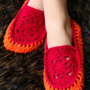 May include: A pair of vibrant red and orange crochet slippers featuring a circular floral motif on the top panel. The slippers are constructed with a bright red center design surrounded by a contrasting orange border with an openwork pattern.