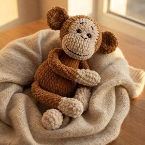 May include: A crocheted monkey stuffed animal featuring a dark brown body, light beige face, ears, hands, and feet. The toy has black embroidered eyes and a stitched mouth, crafted from a soft, textured yarn material with a rounded, plush form.