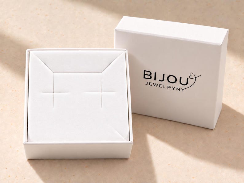 May include: A white square jewelry box with a removable lid featuring the black text BIJOU JEWELRYNY and a heart icon. The open base contains a white insert with two horizontal slits designed for holding earrings or small jewelry items.