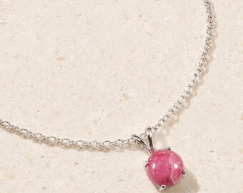 May include: A silver chain necklace featuring a round, polished pink gemstone pendant held in a four-prong setting. The pendant is centered on a delicate link chain, showcasing a smooth, vibrant pink stone with subtle white veining throughout.