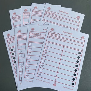 May include: A set of white colour chart cards with red borders and a rose logo. Each card has a section for project name, yarn details, and a colour chart with circles for marking colours.
