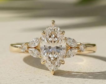 Könnte beinhalten: Ein Goldring mit einem großen, im Marquise-Schliff facettierten Mittelstein, der von sechs Krappen gehalten wird, flankiert von zwei kleineren Marquise-Steinen und einem winzigen runden Stein auf jeder Seite, in einem symmetrischen Design.