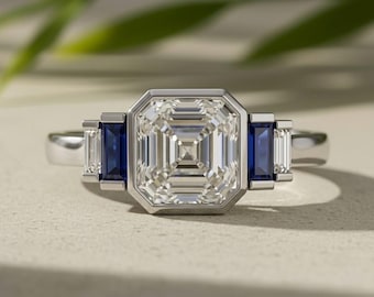 Può includere: Un anello color argento con una grande pietra centrale a taglio quadrato in una montatura a castone, affiancata su ciascun lato da uno zaffiro blu rettangolare e una pietra trasparente rettangolare più piccola.