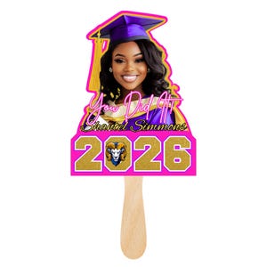 May include: A graduation fan with a pink border, featuring a woman in a cap and gown. The fan has gold glitter text reading "You Did It", "Shantel Simmons 2026". The handle is made of wood.